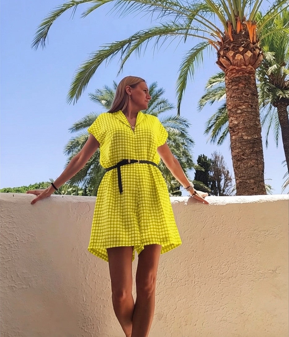 Mujer con vestido corto REVES verde lima de estampado geométrico, cuello solapa y cinturón negro en entorno tropical.